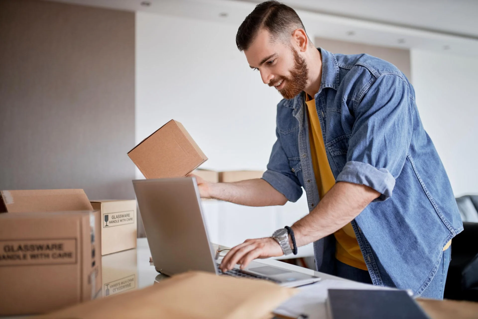 Merchant preparing customer parcels while managing the online store on a laptop