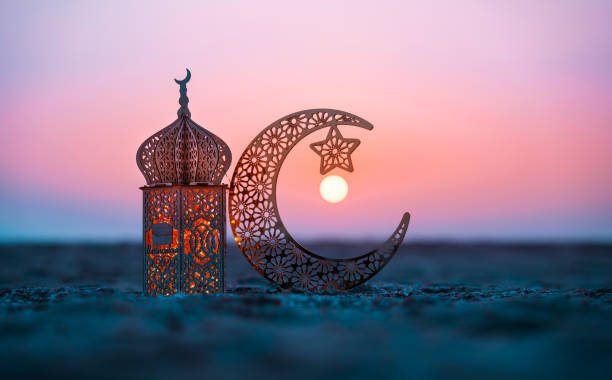 A Ramadan crescent and illuminated lantern at sunset